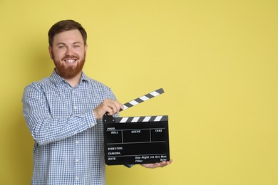 Photo of Making movie. Smiling man with clapperboard on yellow background. Space for text