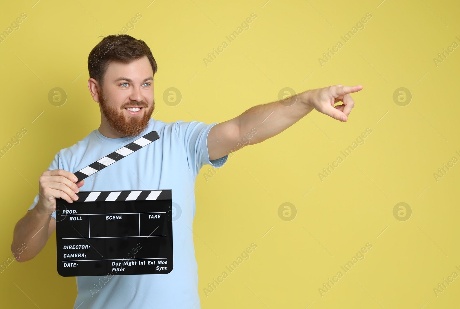 Photo of Making movie. Smiling man with clapperboard pointing at something on yellow background. Space for text