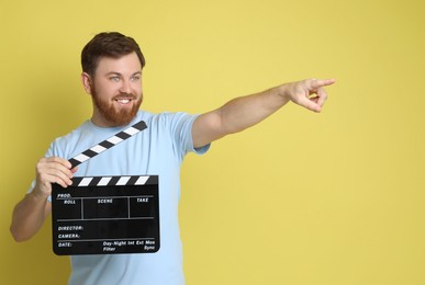 Photo of Making movie. Smiling man with clapperboard pointing at something on yellow background. Space for text