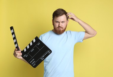 Making movie. Thoughtful man with clapperboard on yellow background