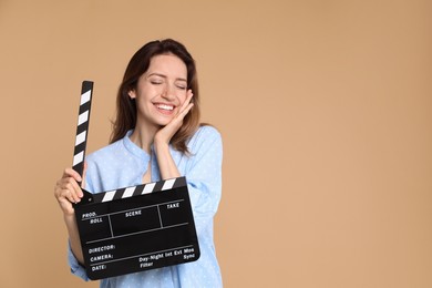 Making movie. Smiling woman with clapperboard on beige background. Space for text