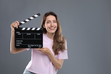 Making movie. Smiling woman with clapperboard on grey background. Space for text
