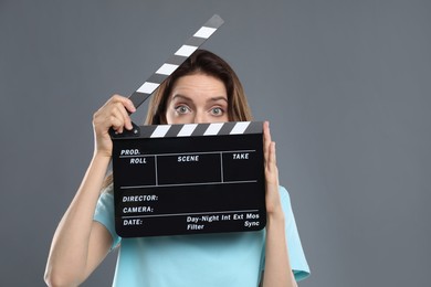 Making movie. Woman with clapperboard on grey background