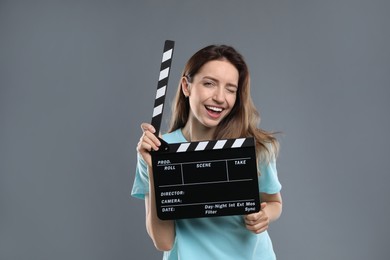Making movie. Smiling woman with clapperboard winking on grey background
