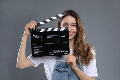 Making movie. Smiling woman with clapperboard on grey background