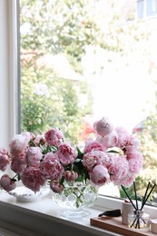 Beautiful pink peonies in vase on window sill, space for text. Interior design
