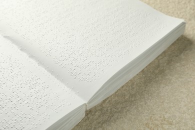 Photo of Book with Braille text on beige textured table, closeup. Education and leisure for blind people