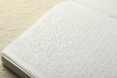 Book with Braille text on beige textured table, closeup. Education and leisure for blind people