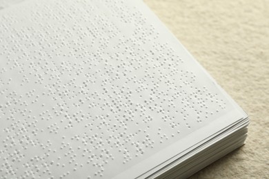 Book with Braille text on beige textured table, closeup. Education and leisure for blind people