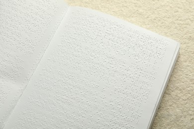 Book with Braille text on beige textured table, top view. Education and leisure for blind people