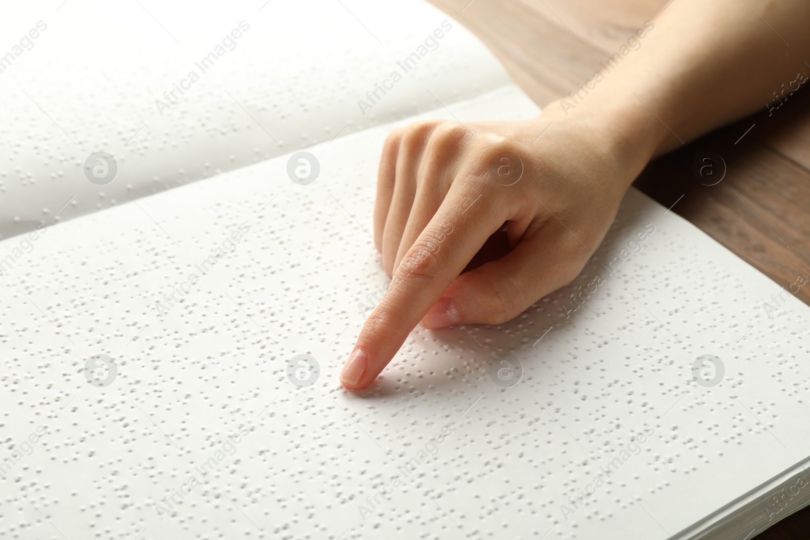 Photo of Blind woman reading book written in Braille at wooden table, closeup