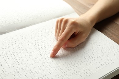 Photo of Blind woman reading book written in Braille at wooden table, closeup