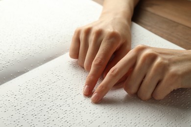 Photo of Blind woman reading book written in Braille at wooden table, closeup