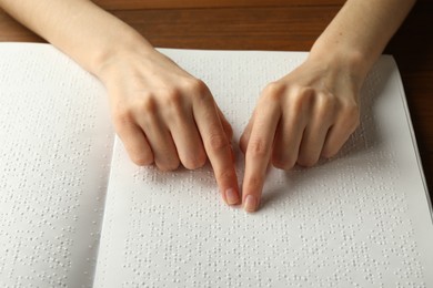 Blind woman reading book written in Braille at wooden table, closeup