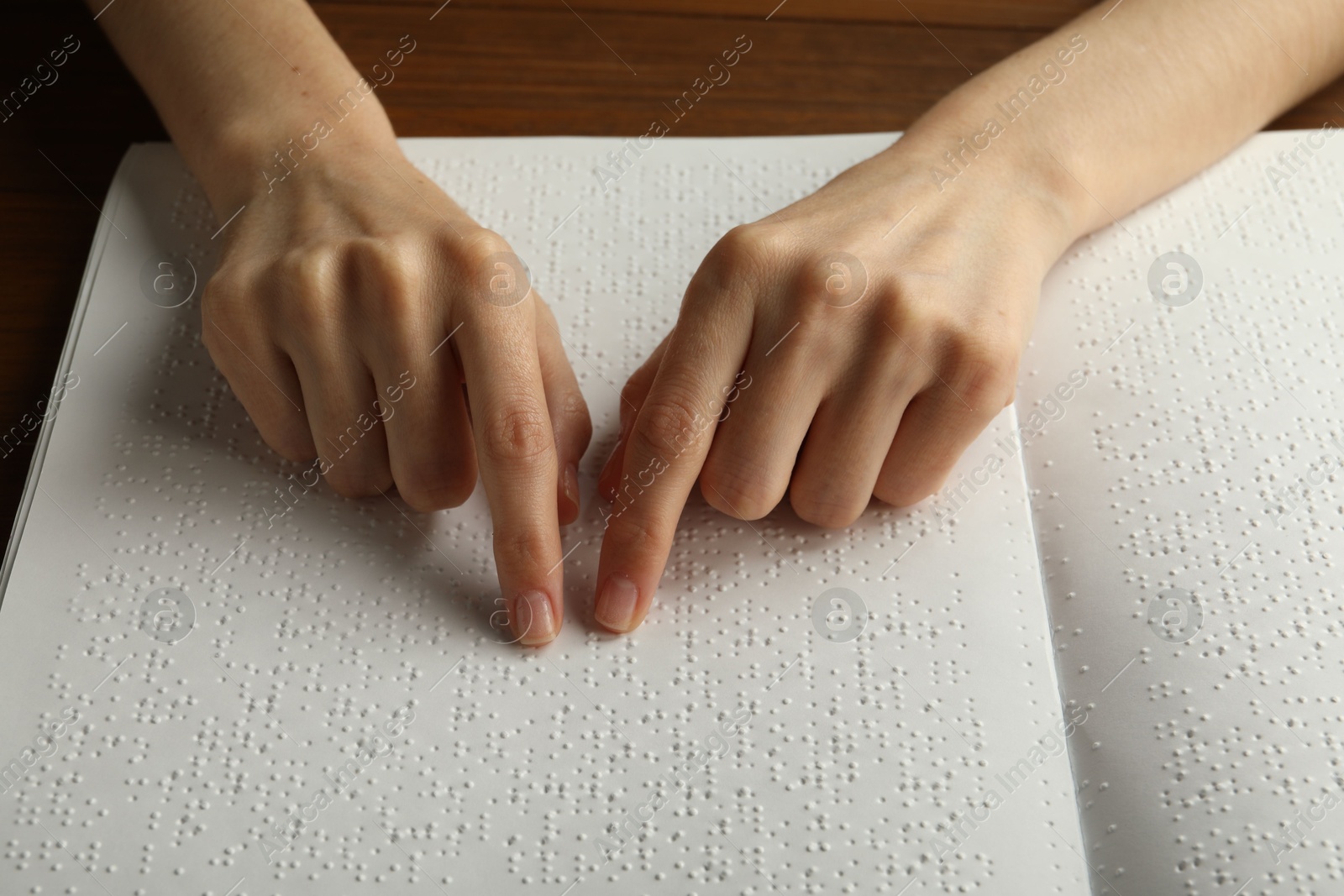 Photo of Blind woman reading book written in Braille at wooden table, closeup