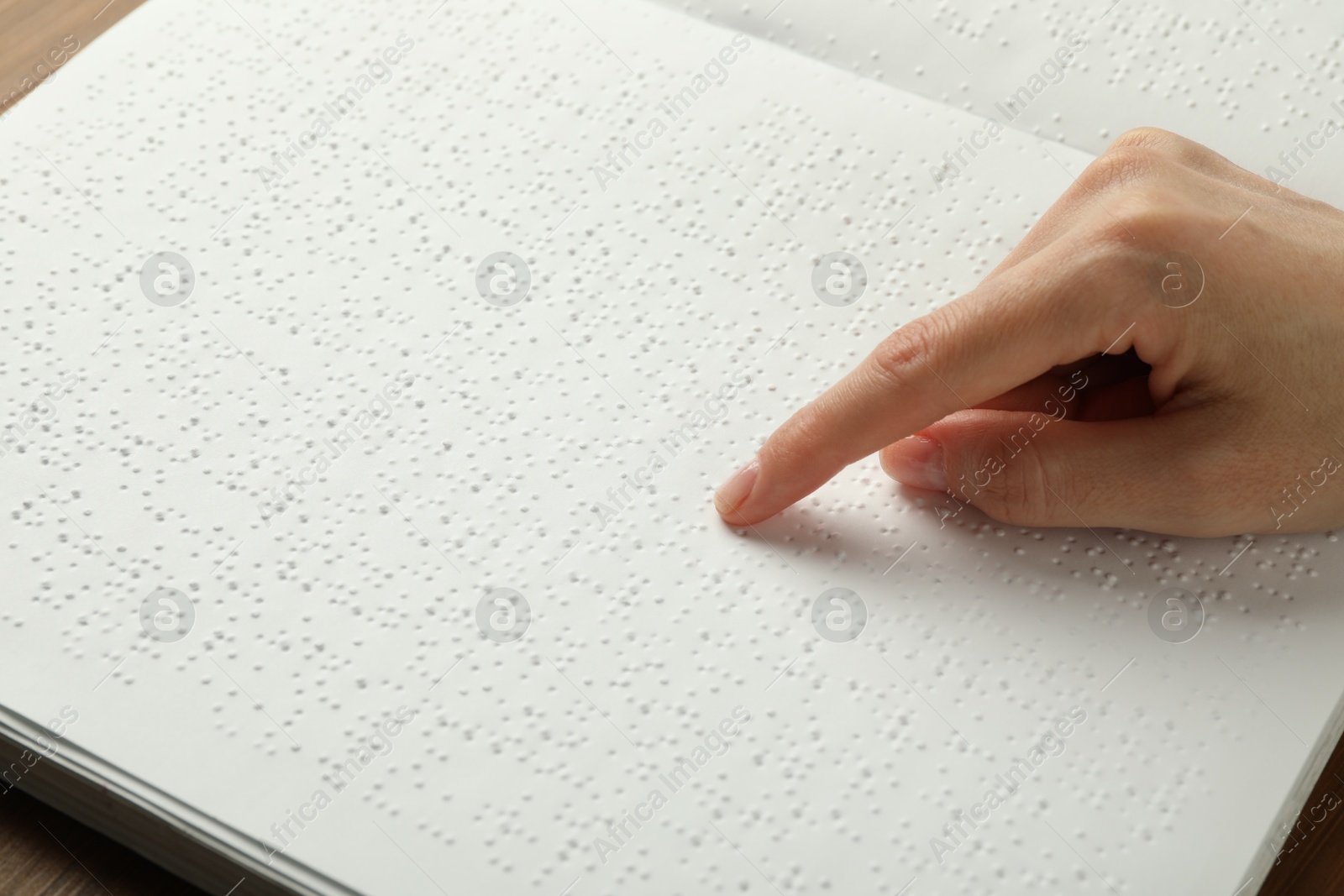 Photo of Blind woman reading book written in Braille at table, closeup