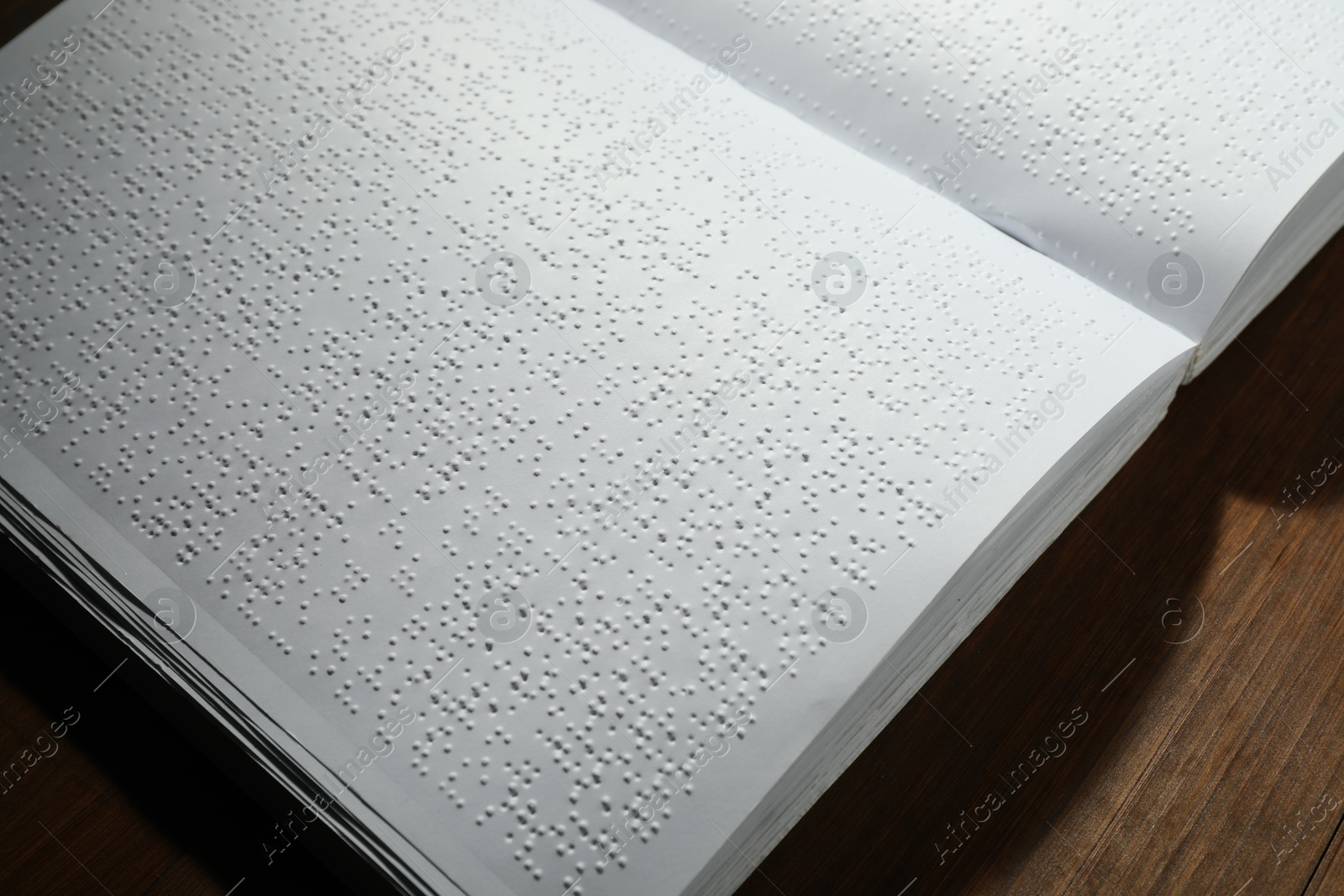 Photo of Book with Braille text on wooden table, closeup. Education and leisure for blind people