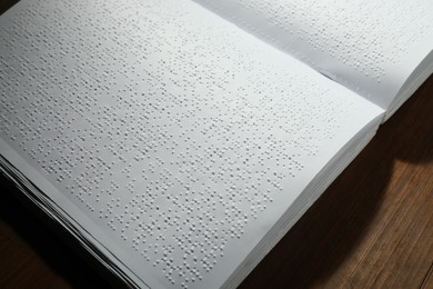 Photo of Book with Braille text on wooden table, closeup. Education and leisure for blind people