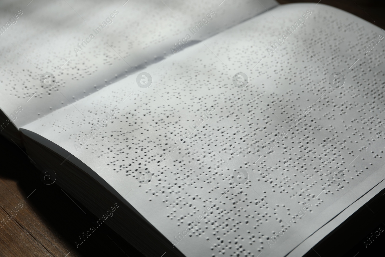 Photo of Book with Braille text on wooden table, closeup. Education and leisure for blind people