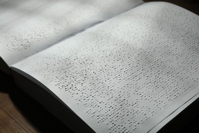 Book with Braille text on wooden table, closeup. Education and leisure for blind people