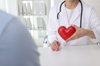Photo of Doctor showing red heart to patient at white table in clinic, closeup