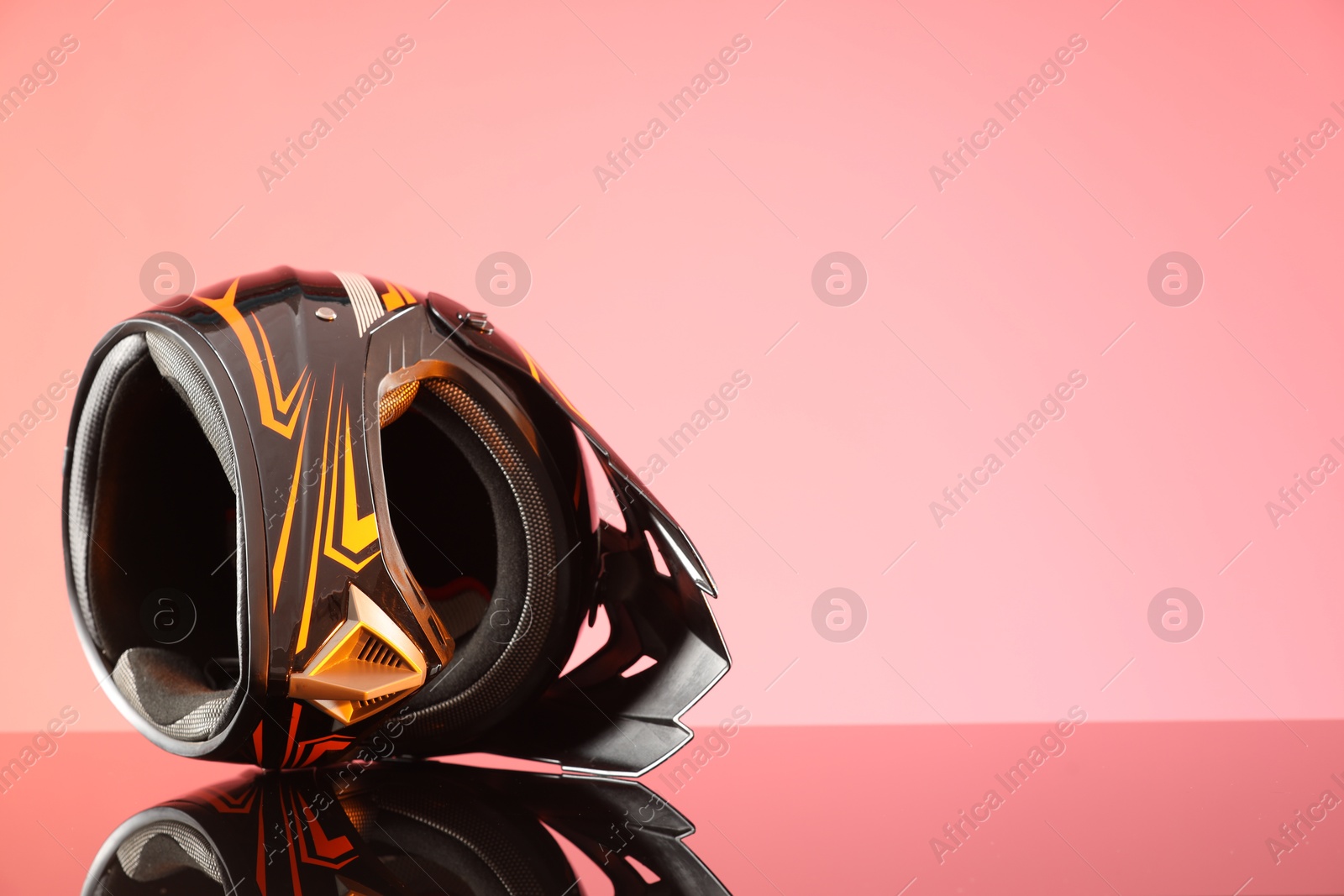 Photo of Modern motorcycle helmet with visor on mirror surface against pink background. Space for text