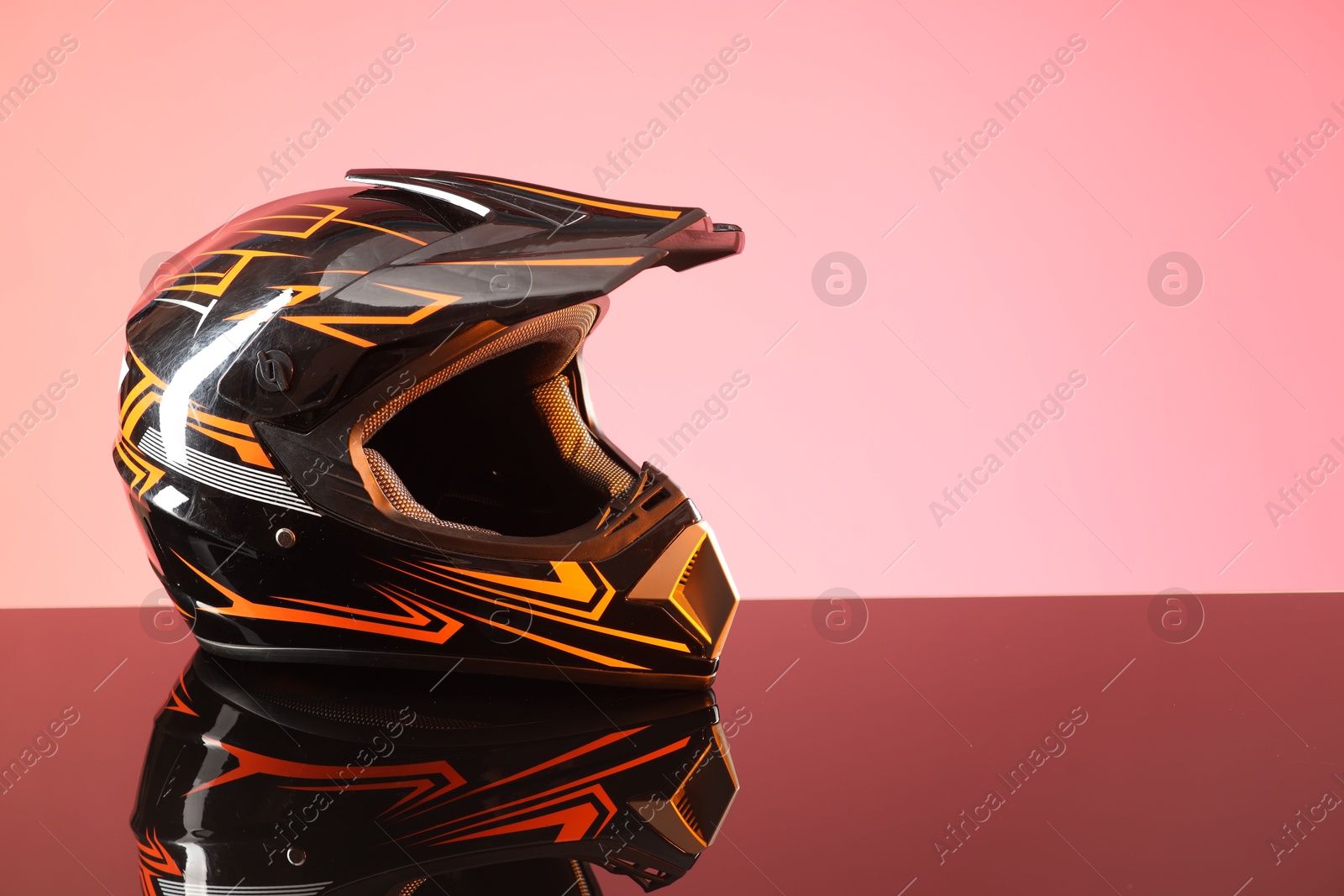 Photo of Modern motorcycle helmet with visor on mirror surface against pink background. Space for text