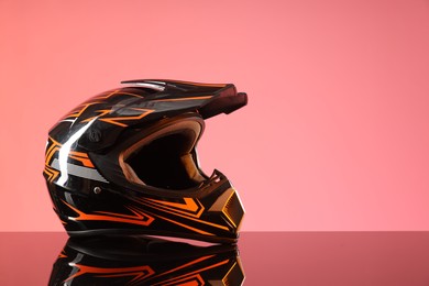 Modern motorcycle helmet with visor on mirror surface against pink background. Space for text