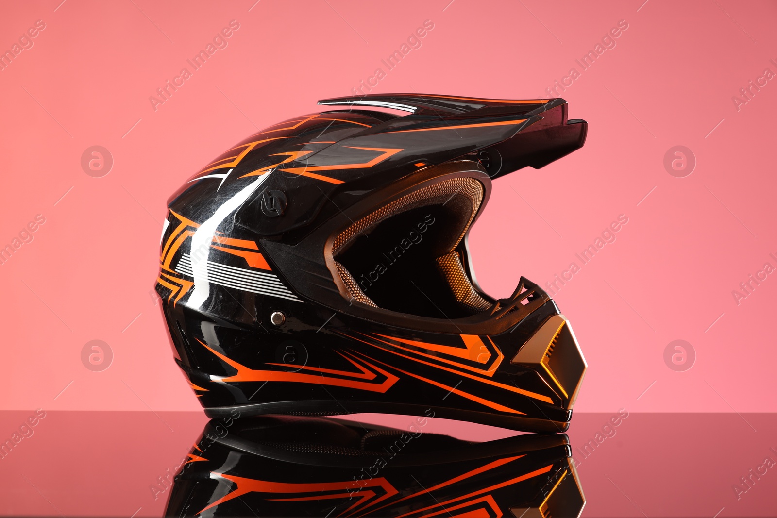 Photo of Modern motorcycle helmet with visor on mirror surface against pink background