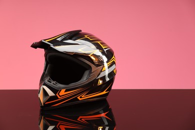 Photo of Modern motorcycle helmet with visor on mirror surface against pink background. Space for text