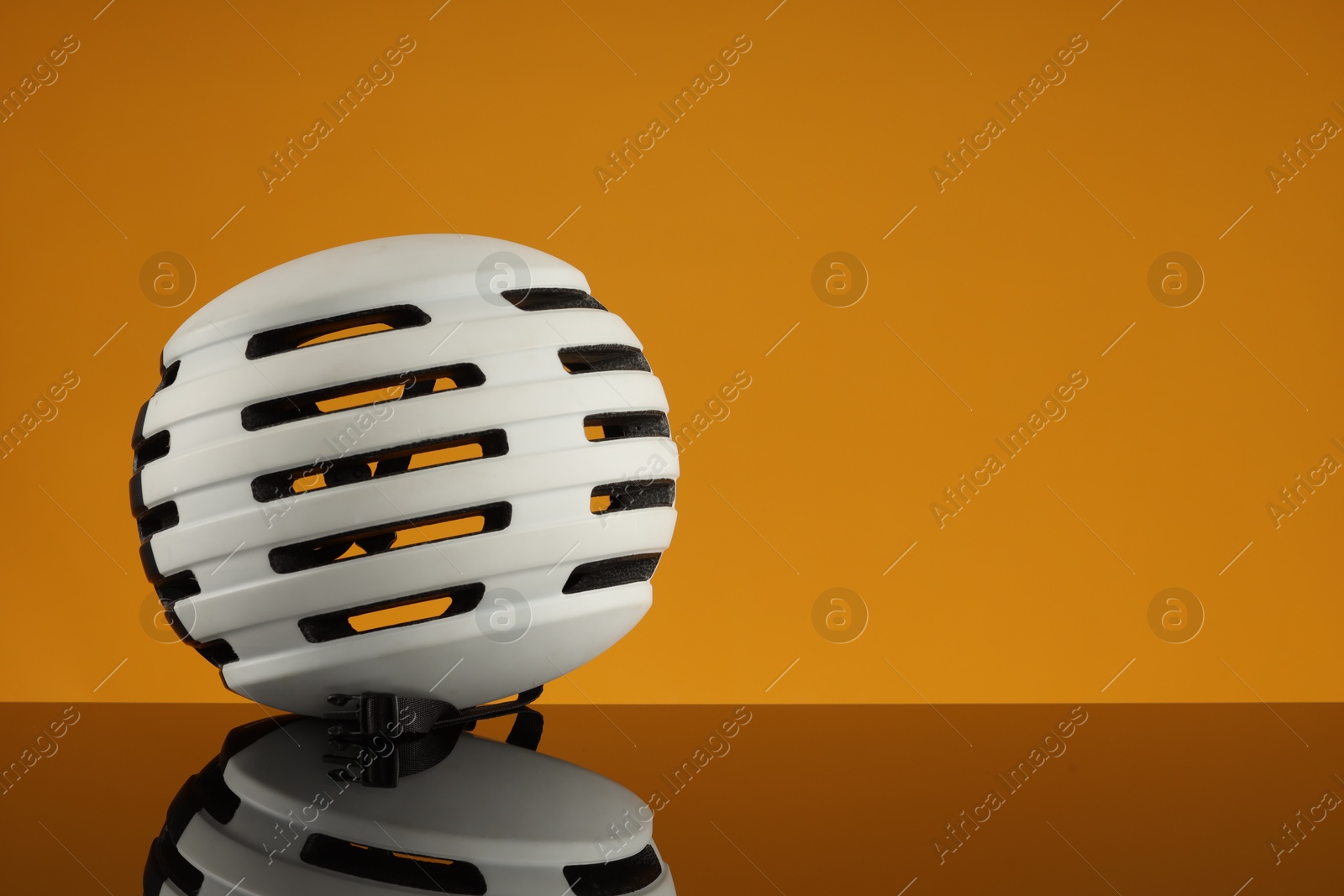 Photo of White protective helmet on mirror surface against orange background. Space for text