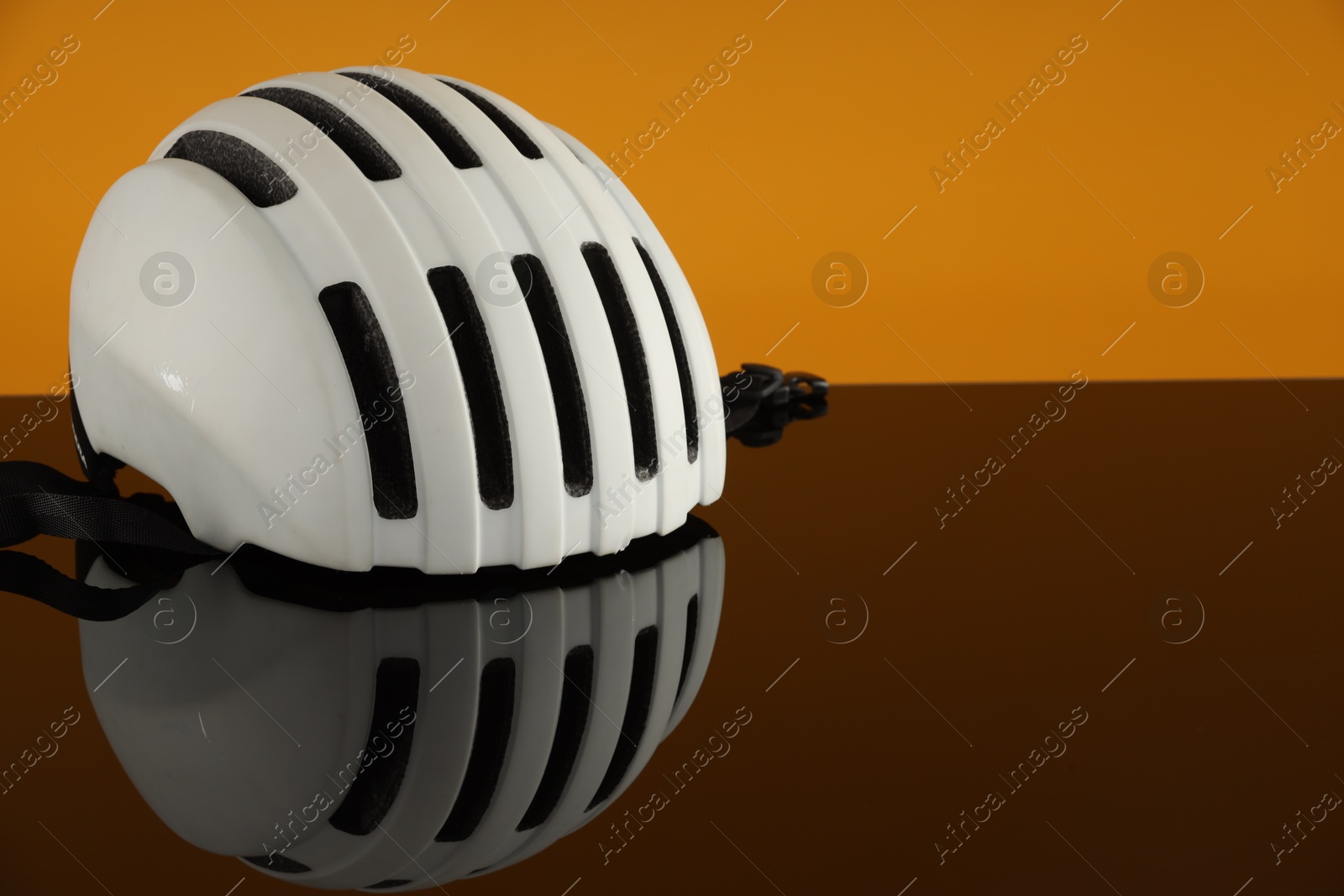 Photo of White protective helmet on mirror surface against orange background. Space for text