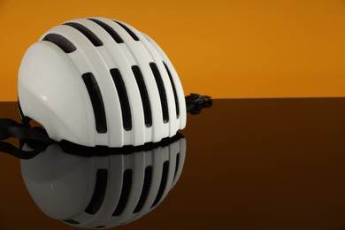 White protective helmet on mirror surface against orange background. Space for text