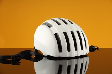 Photo of White protective helmet on mirror surface against orange background