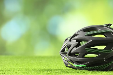 Stylish protective helmet on green grass against blurred background. Space for text