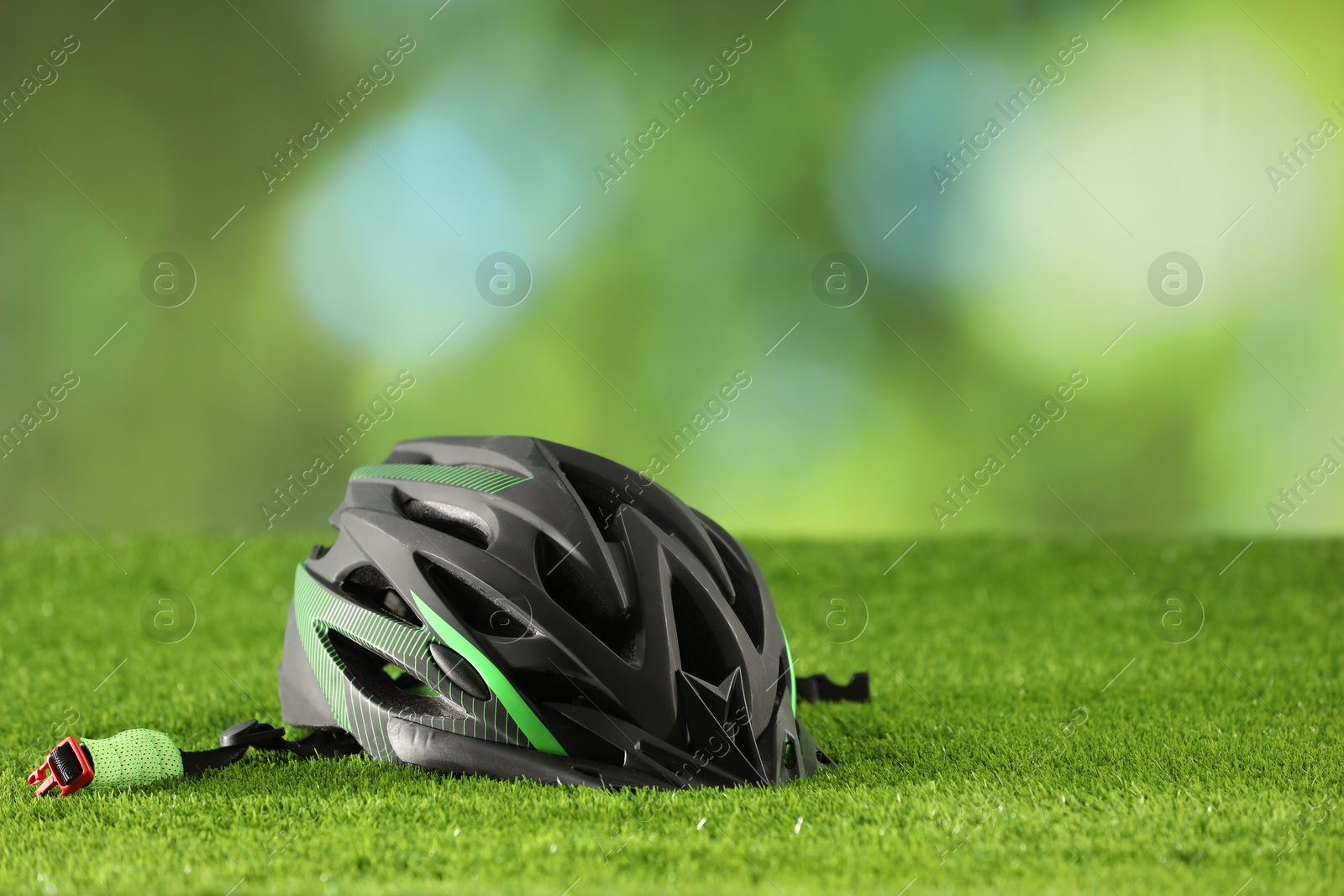 Photo of Stylish protective helmet on green grass against blurred background. Space for text