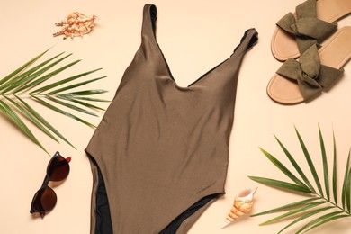 Photo of Beautiful swimsuit, palm leaves, sunglasses and slippers on beige background, flat lay