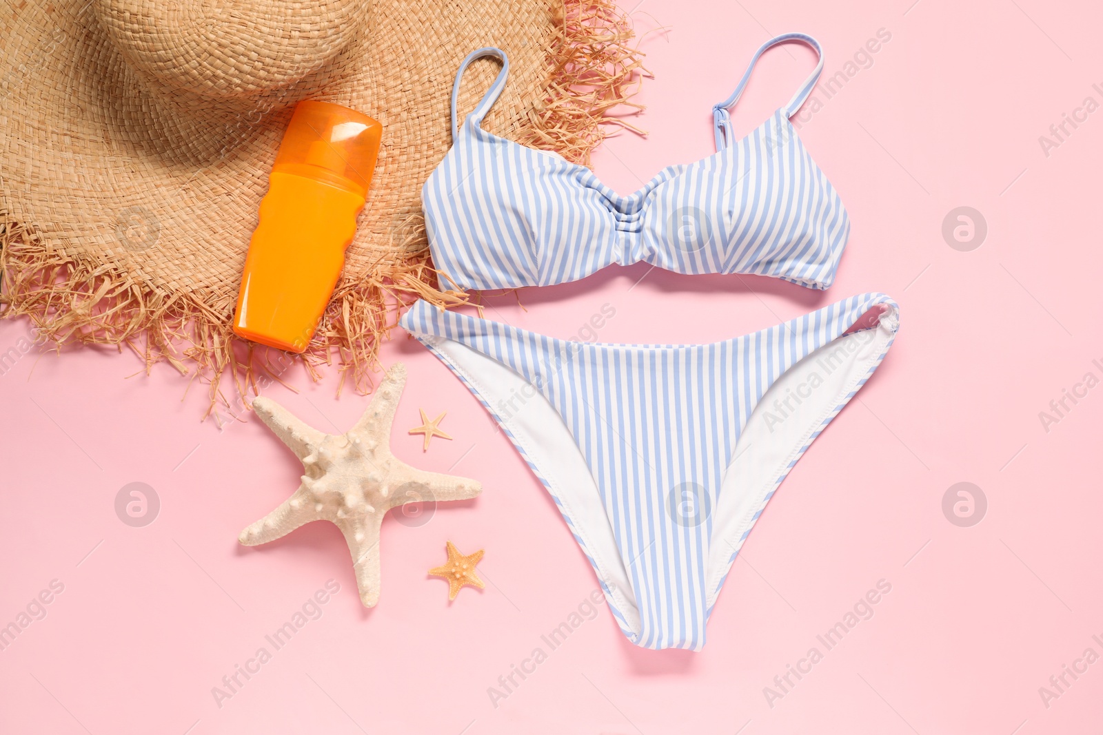 Photo of Striped swimsuit, sunscreen, hat and starfishes on pink background, flat lay