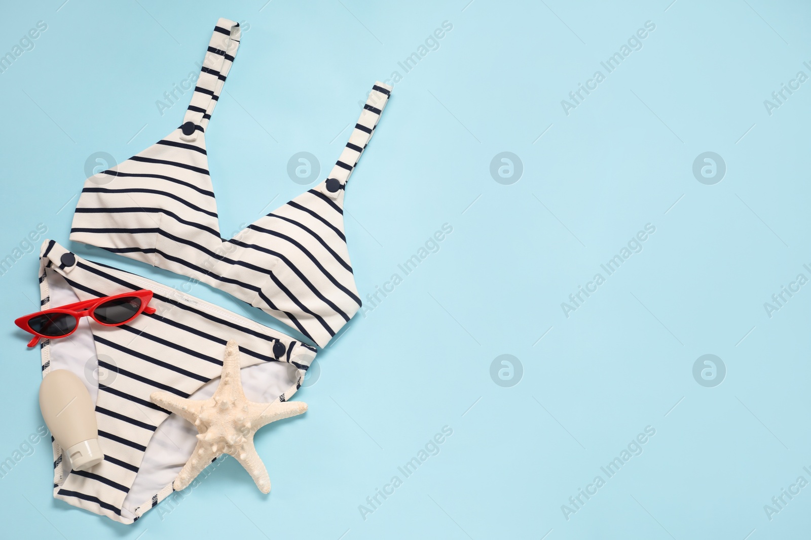 Photo of Striped swimsuit, sunglasses and starfish on light blue background, flat lay. Space for text