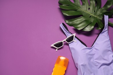 Flat lay composition with beautiful swimsuit, sunscreen and sunglasses on purple background. Space for text