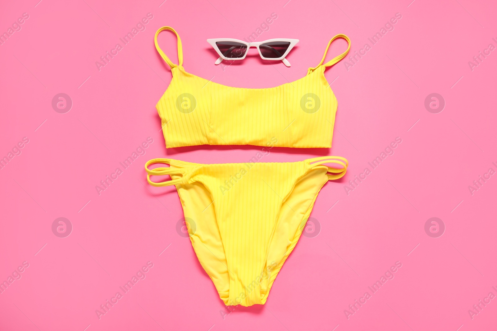 Photo of Yellow swimsuit and sunglasses on pink background, flat lay