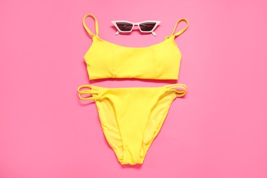 Photo of Yellow swimsuit and sunglasses on pink background, flat lay
