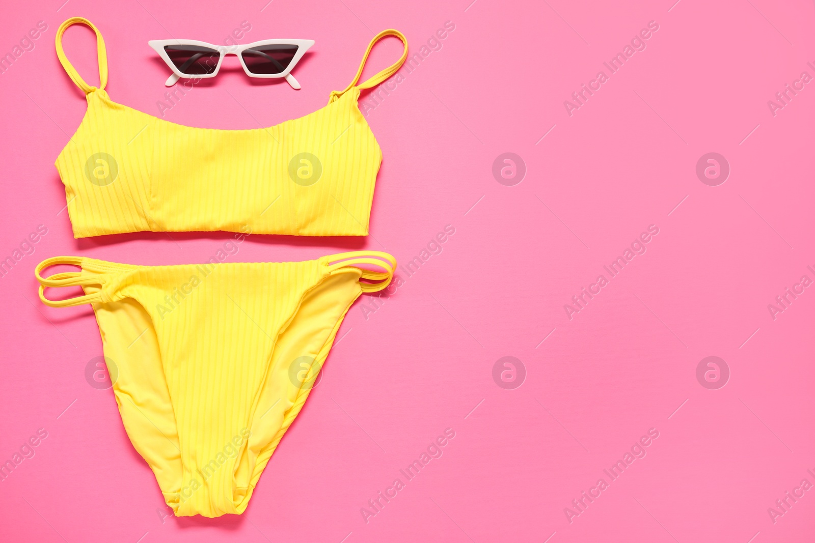 Photo of Yellow swimsuit and sunglasses on pink background, flat lay. Space for text