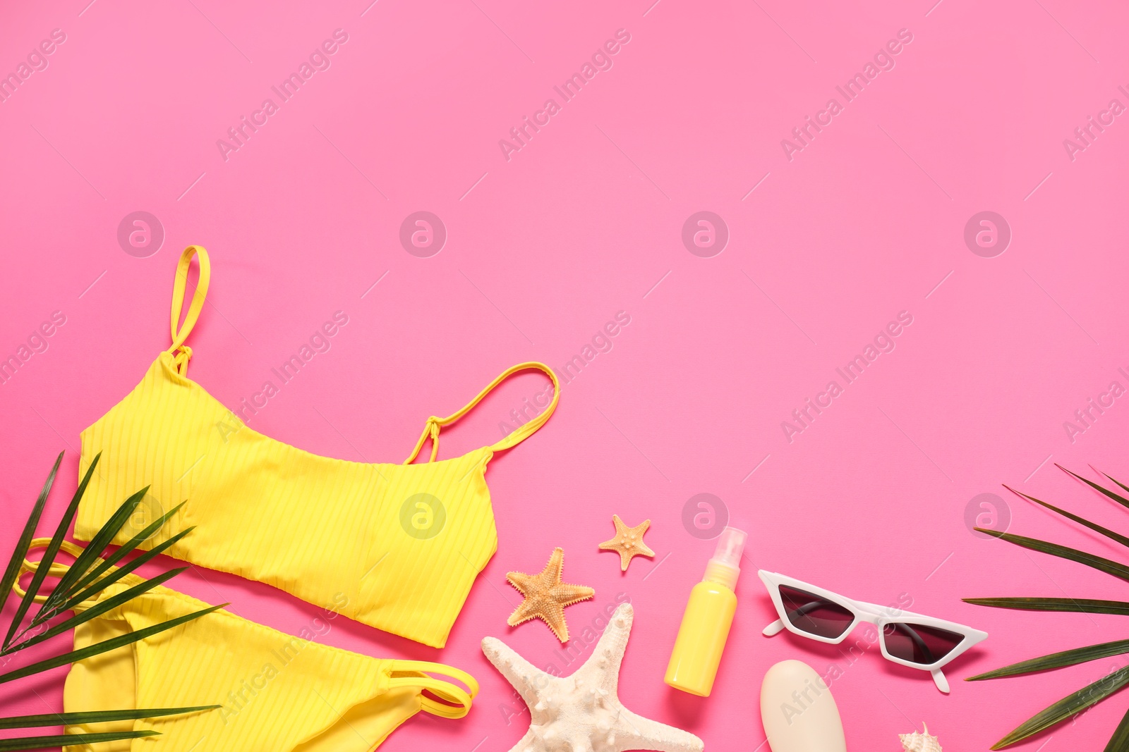 Photo of Flat lay composition with yellow swimsuit, sunscreen and sunglasses on pink background. Space for text
