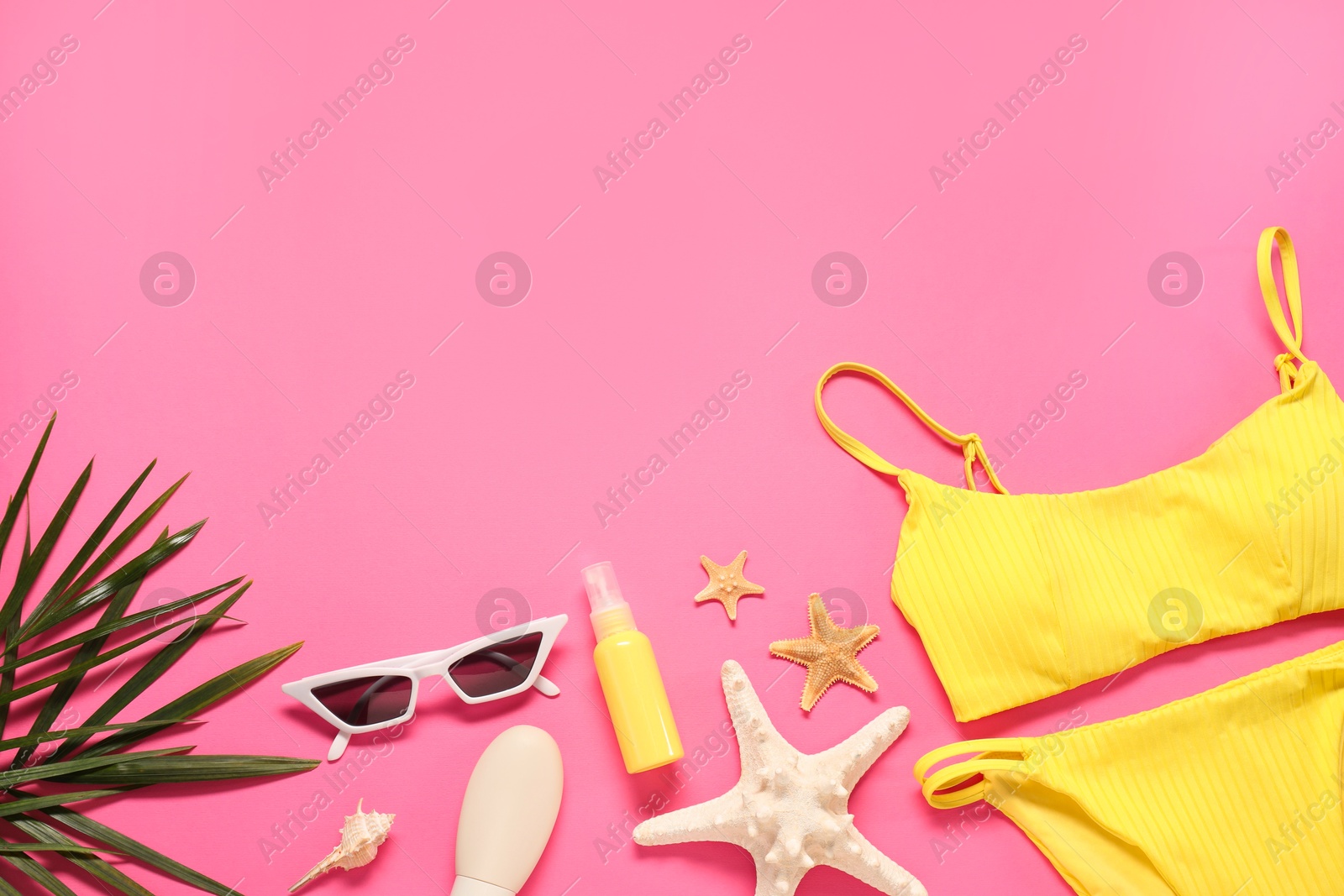 Photo of Flat lay composition with yellow swimsuit, sunscreen and sunglasses on pink background. Space for text