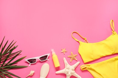 Flat lay composition with yellow swimsuit, sunscreen and sunglasses on pink background. Space for text