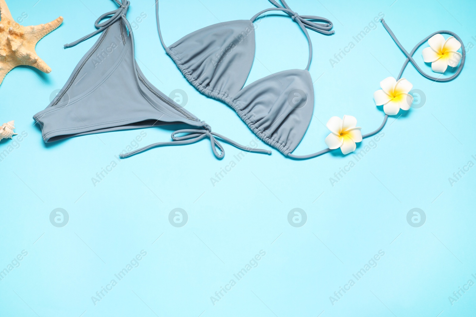 Photo of Flat lay composition with beautiful swimsuit, flowers and starfish on light blue background. Space for text