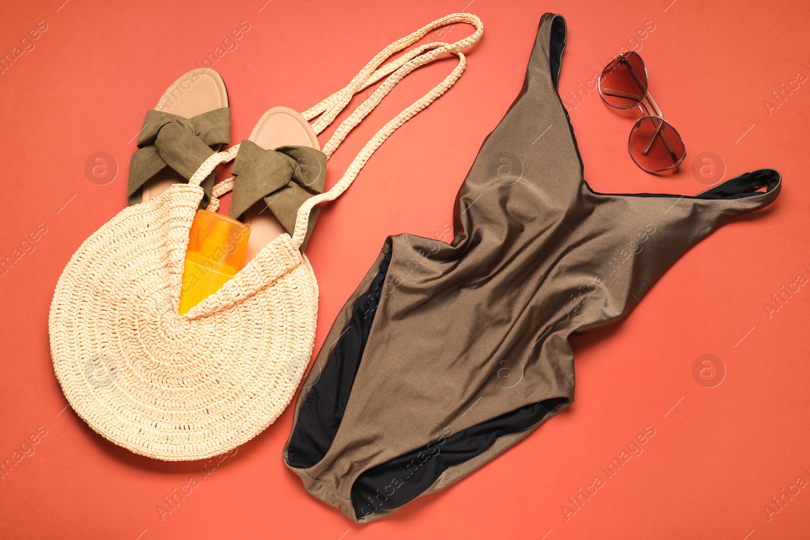 Photo of Beautiful swimsuit, bag, sunscreen, slippers and sunglasses on coral background, flat lay