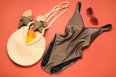 Beautiful swimsuit, bag, sunscreen, slippers and sunglasses on coral background, flat lay