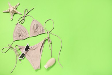 Photo of Beige swimsuit, sunglasses, starfish and sunscreen on green background, flat lay. Space for text